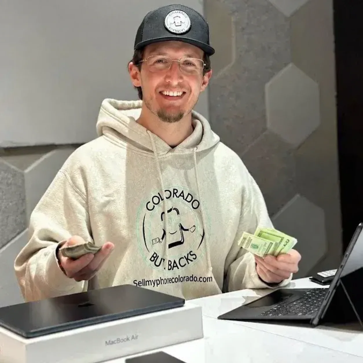 Riley, owner of Sell My Phone Colorado, at the counter with cash in hand